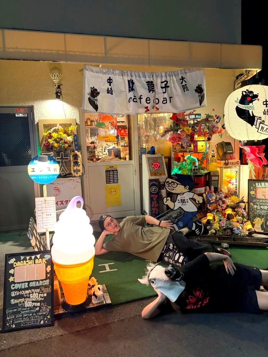 夜のエンスの店先。提灯と看板の前で、お客さんが寝転んでくつろぐ様子
